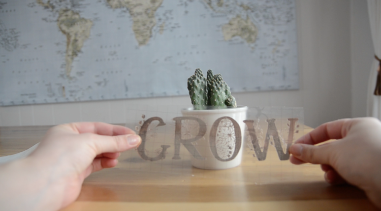 using transfer tape to apply the intricate floral lettering to a plant pot- design cut out of matte adhesive foil