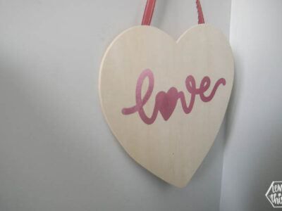 Hanging wood sign in heart shape with pink foil script that reads 'love'