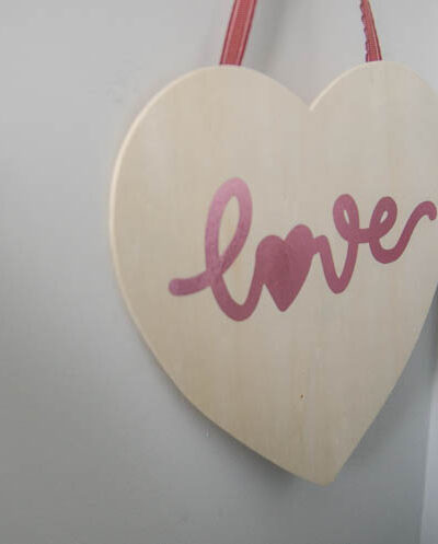 Hanging wood sign in heart shape with pink foil script that reads 'love'