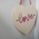 Hanging wood sign in heart shape with pink foil script that reads 'love'