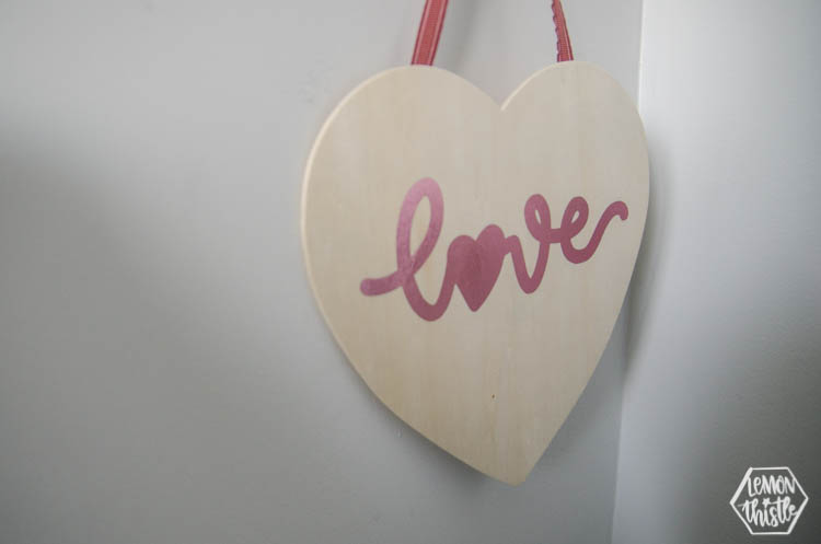 Hanging wood sign in heart shape with pink foil script that reads 'love'