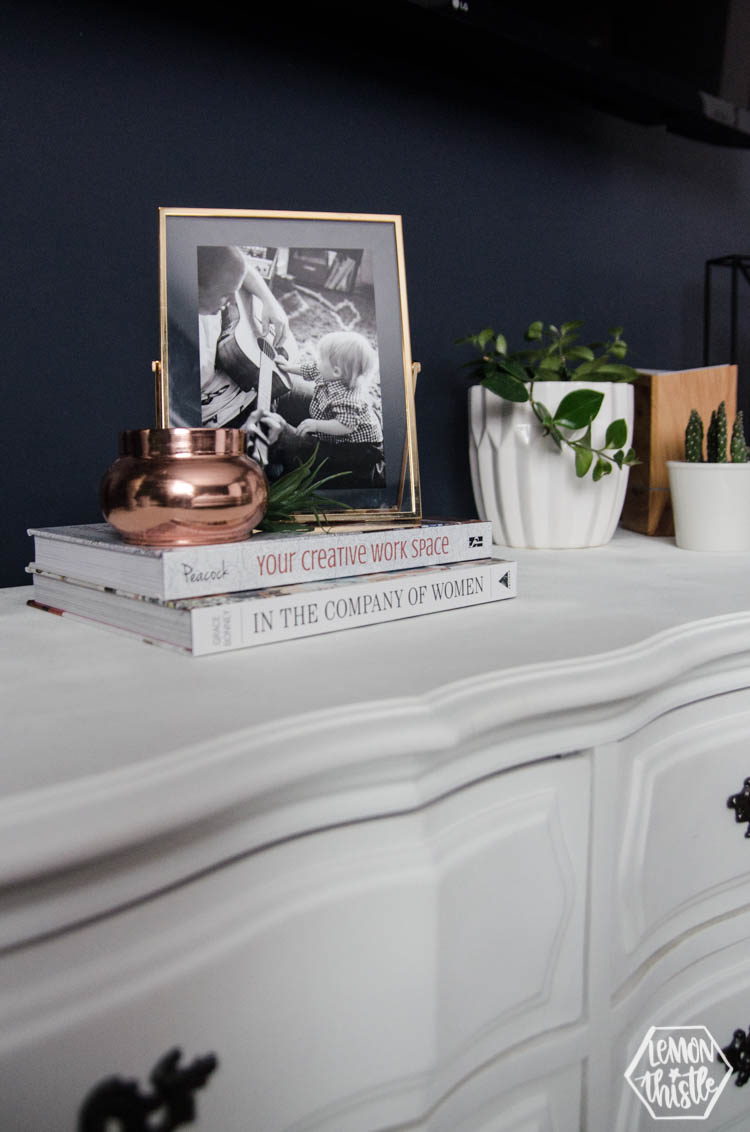 stacked books with candle, faux airplant and photo frame on top of dresser