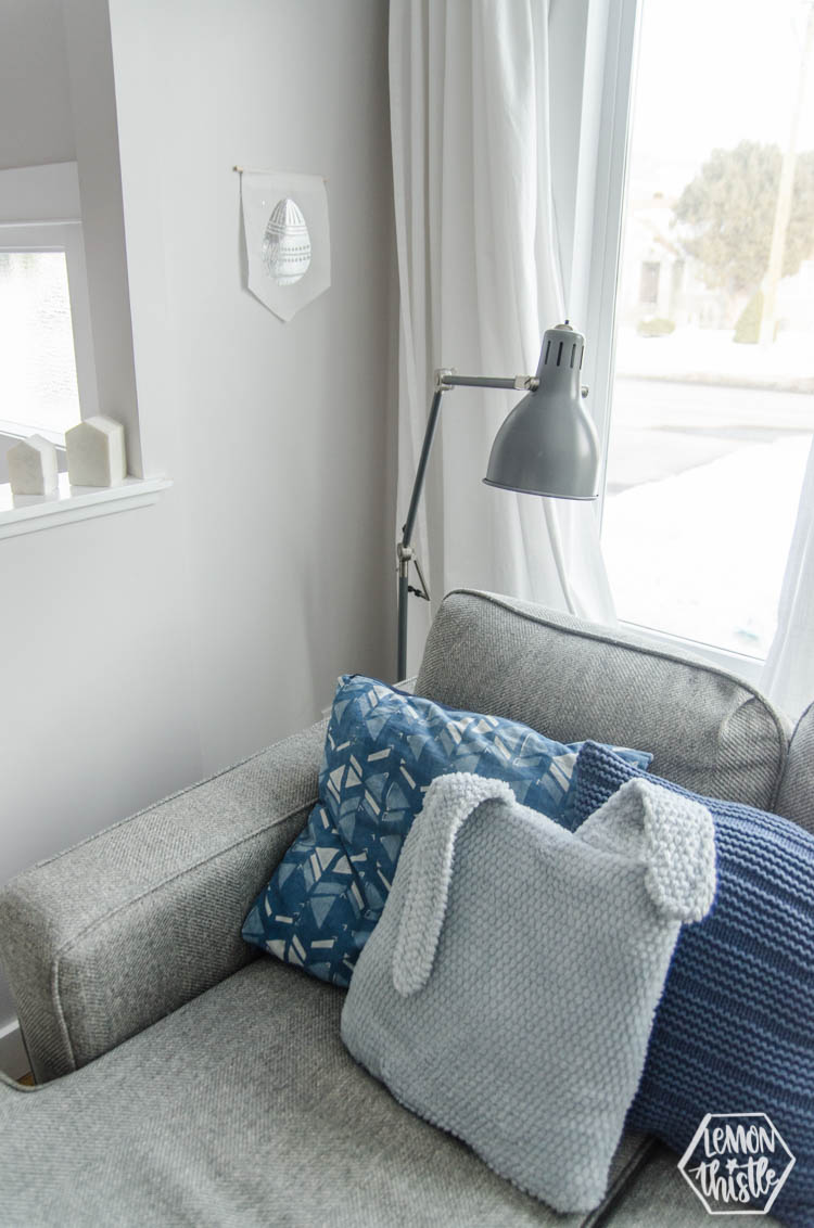 bunny ears pillow on couch, easter egg pennant on wall in a living room corner
