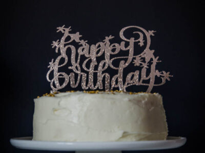 Happy Birthday glittery cake topper on white iced cake