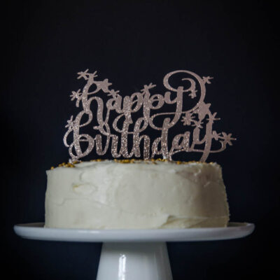 Happy Birthday glittery cake topper on white iced cake