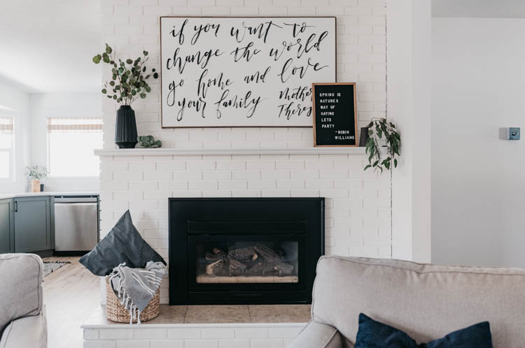 white brick fireplace decorated with black vases and white details, hand lettered art and letterboard reads 'spring is nature's way of saying let's party' - robin williams quote