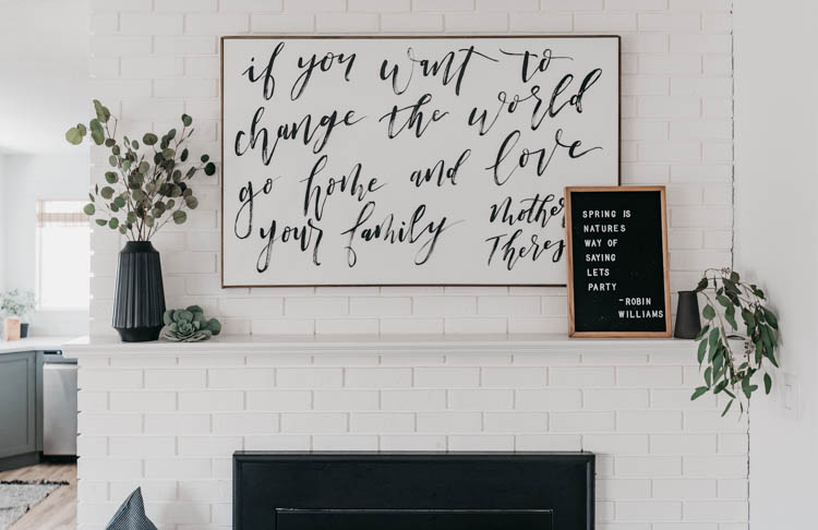 white brick fireplace decorated with black vases and white details, hand lettered art and letterboard reads 'spring is nature's way of saying let's party' - robin williams quote