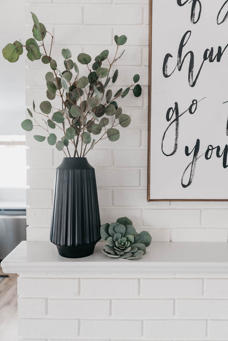 Black vase full of silver dollar eucalyptus on white brick fireplace