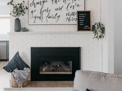white brick fireplace decorated with black vases and white details, hand lettered art and letterboard reads 'spring is nature's way of saying let's party' - robin williams quote