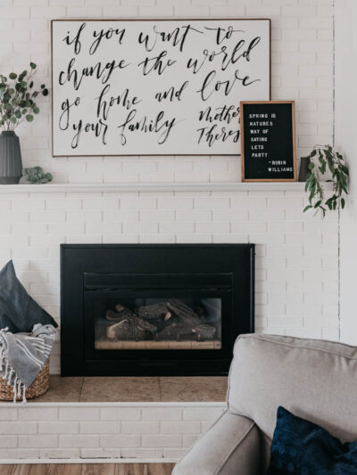 white brick fireplace decorated with black vases and white details, hand lettered art and letterboard reads 'spring is nature's way of saying let's party' - robin williams quote