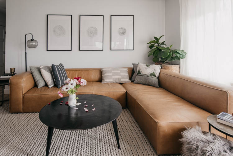 Modern living room with a camel leather sectional and round coffee table... and tree ring art!