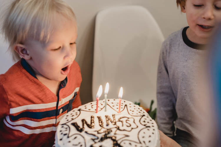 three year old blowing out candles on his super hero cake