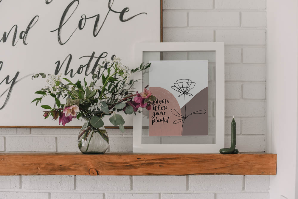 hand lettered modern art reads 'bloom where you are planted' in frame on mantel
