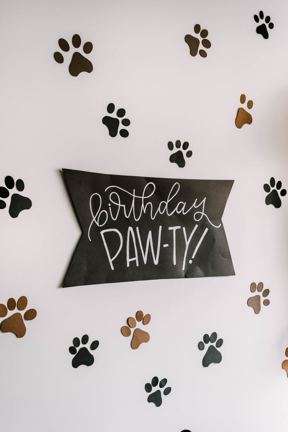 Puppy themed party decor- black poster board sign reads birthday 'paw-ty' surrounded by paw prints on wall