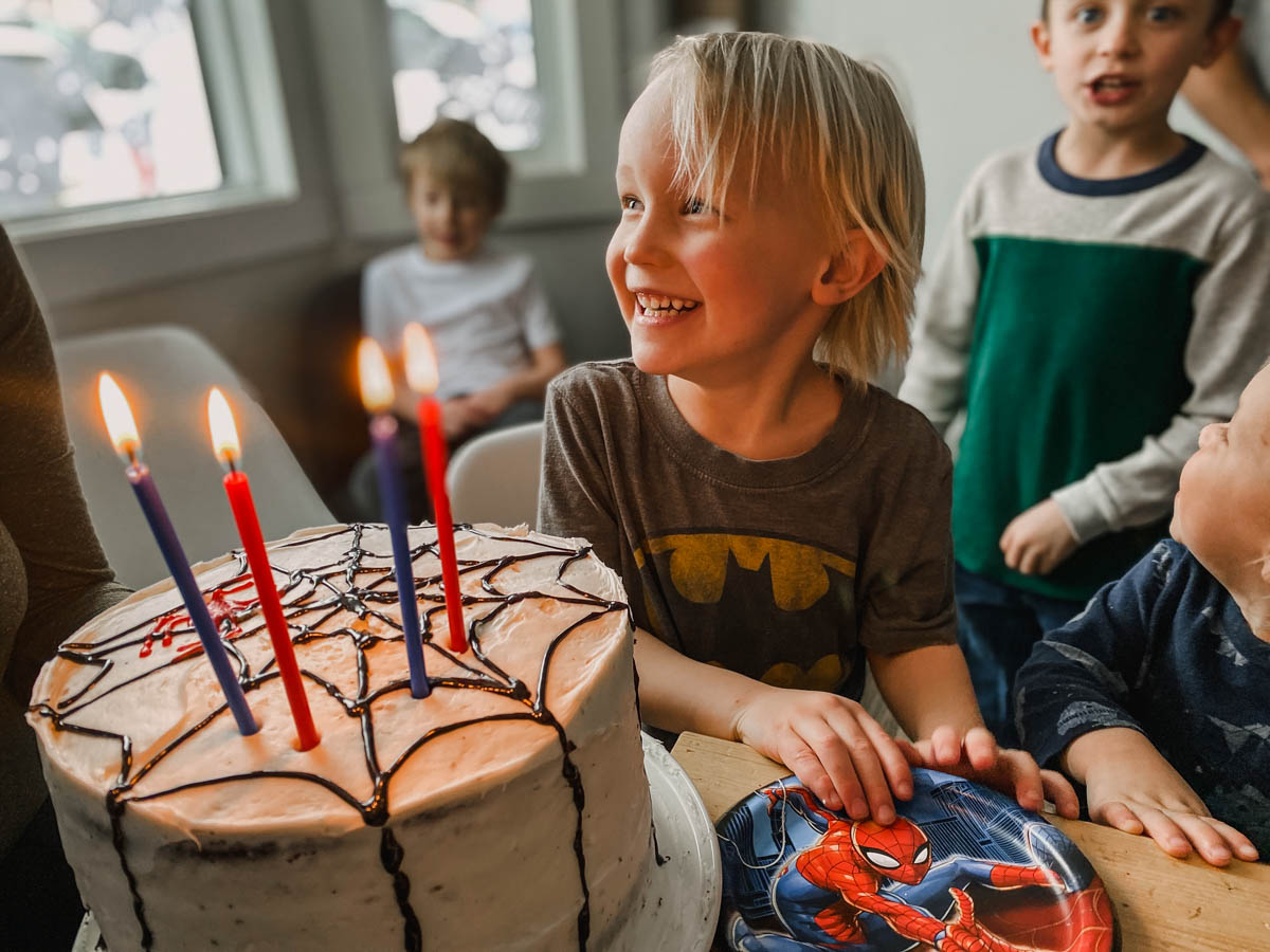 boy blowing out candles on a spiderman cake