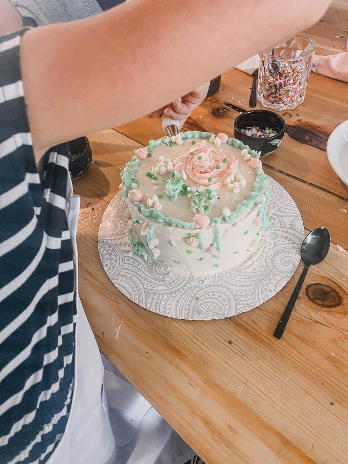 Girl decorating a cake with green and pink icing at a cake decorating birthday party 