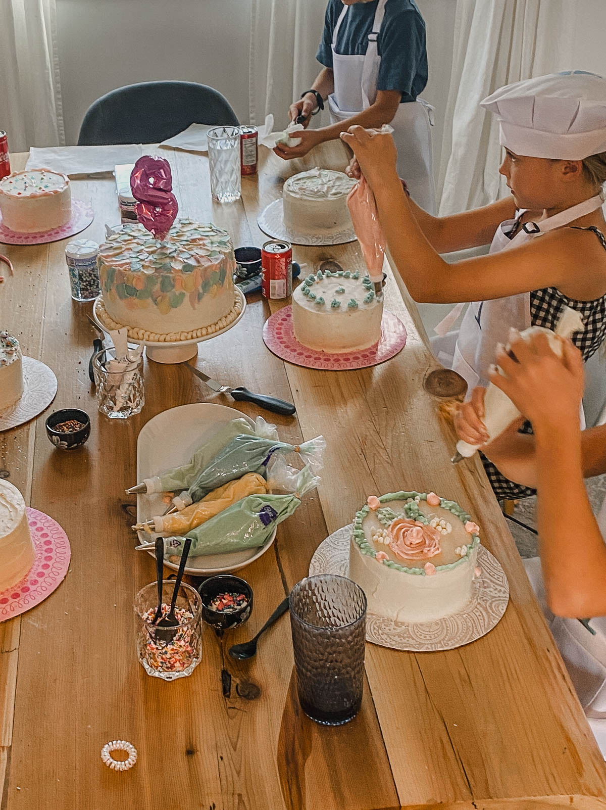Kids decorating cakes at a birthday party, table full of icing, sprinkles and cakes