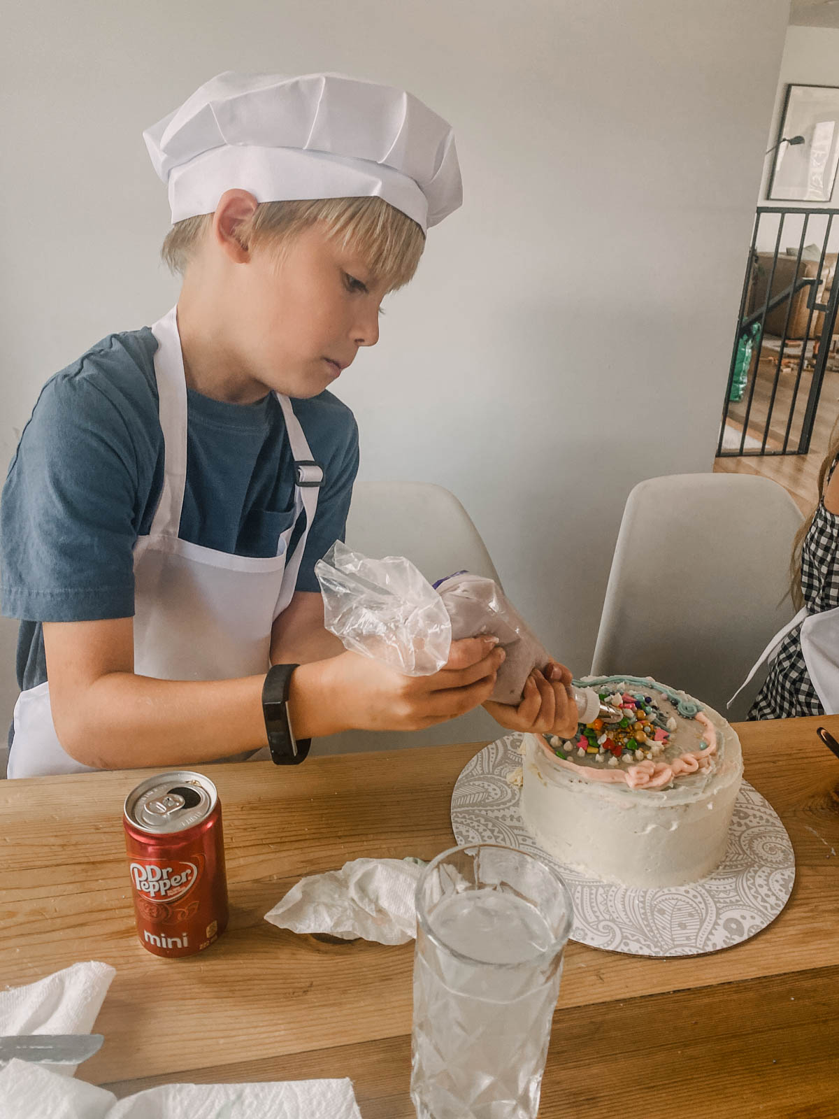 Boy decorating a cake at a cake decorating party wearing an apron and chefs hat