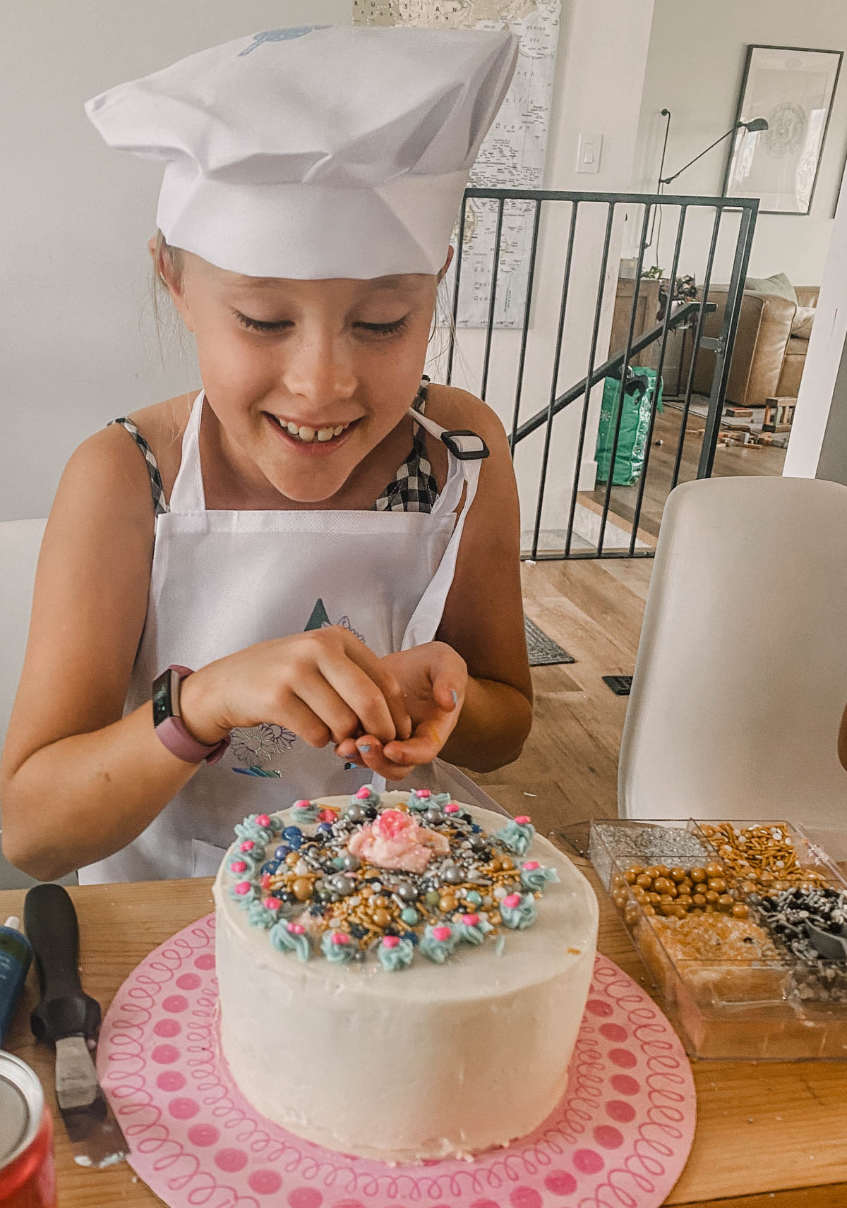 Girl decorating a cake with sprinkles, wearing a chefs hat and apron at a girls birthday cake decorating party