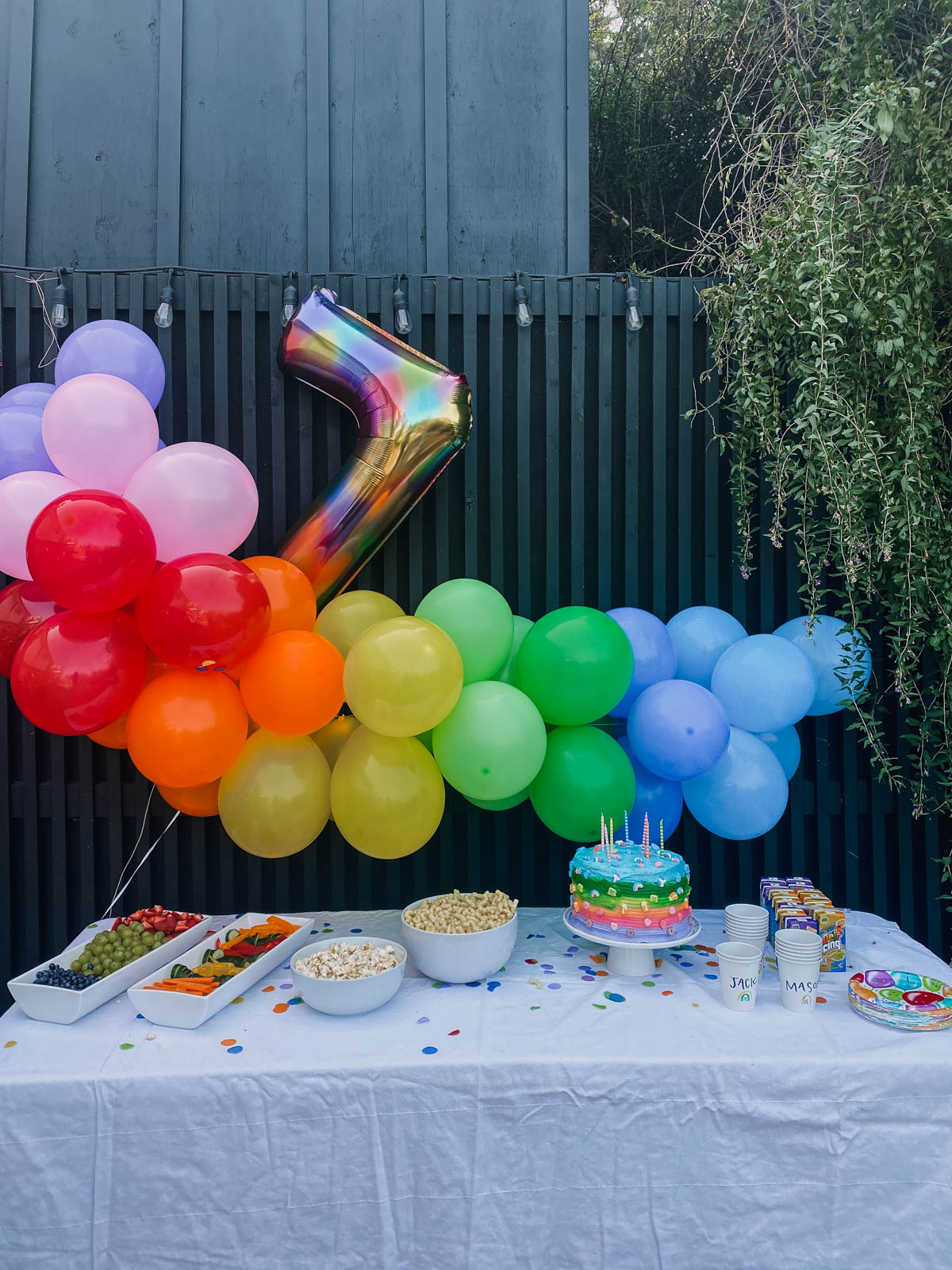 rainbow birthday party theme- rainbow balloon garland against a black wall over a party table