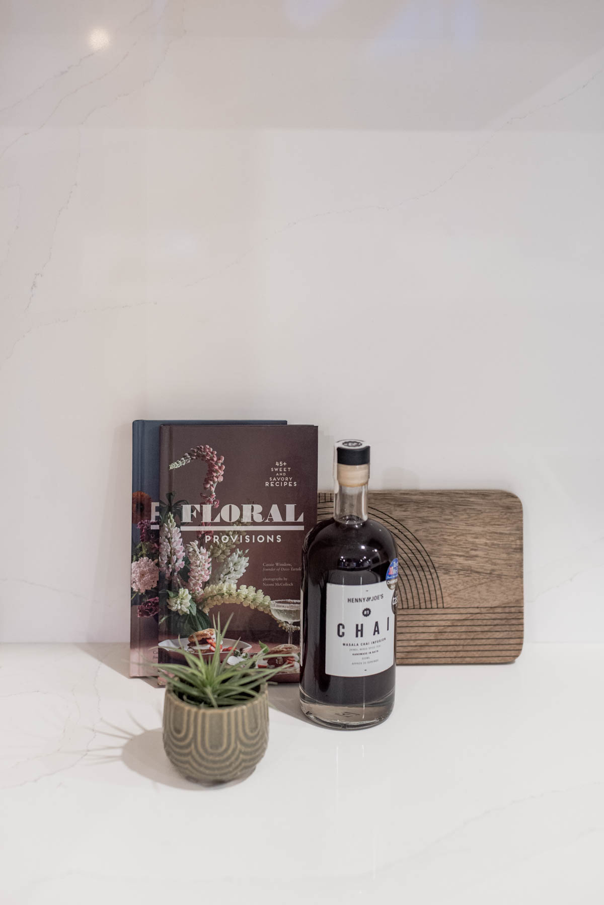 Countertop vignette with floral cookbooks, wood board, chai syrup and plant