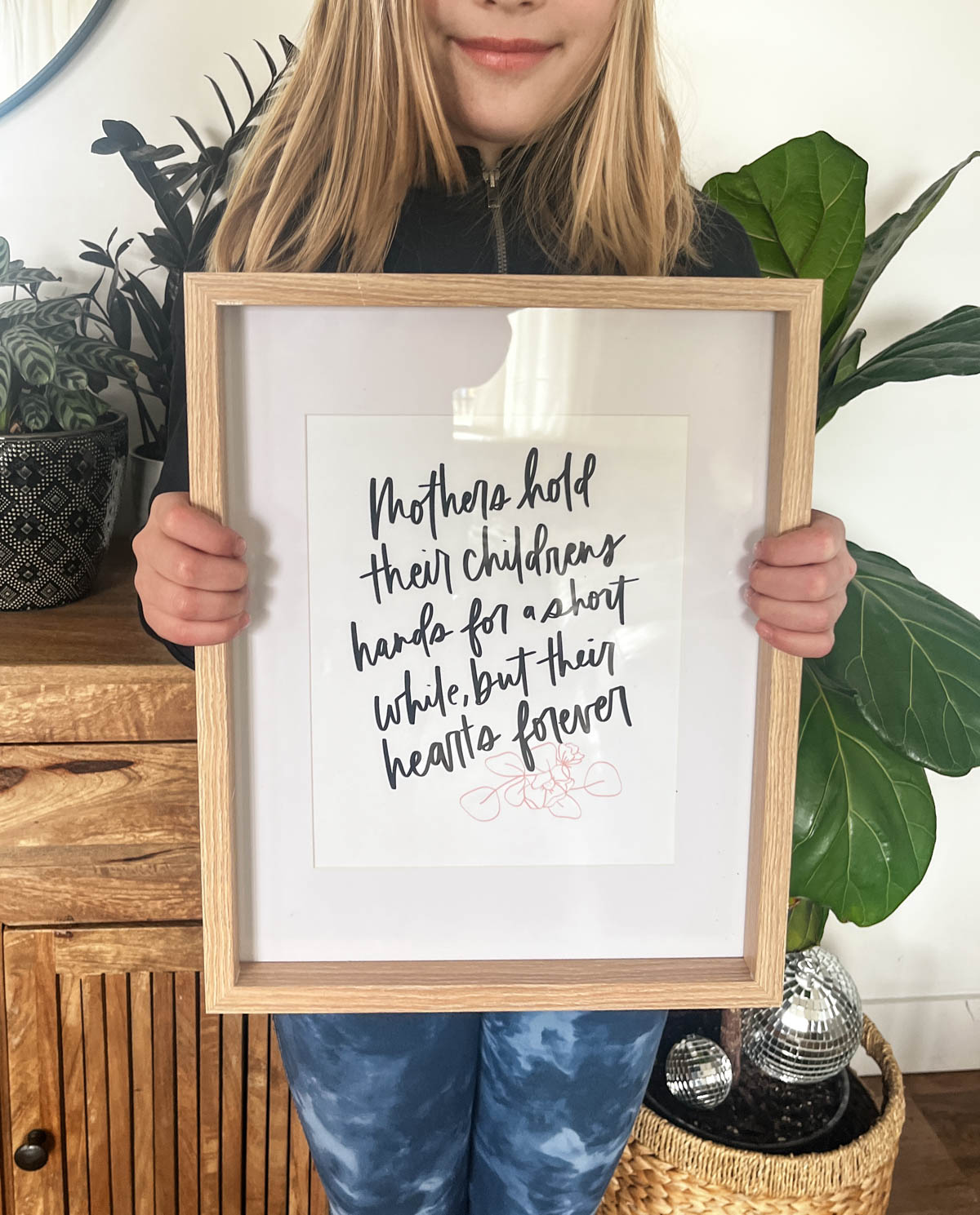 hand lettered quote about motherhood framed in a light wood picture frame. Girl holding it as a gift.