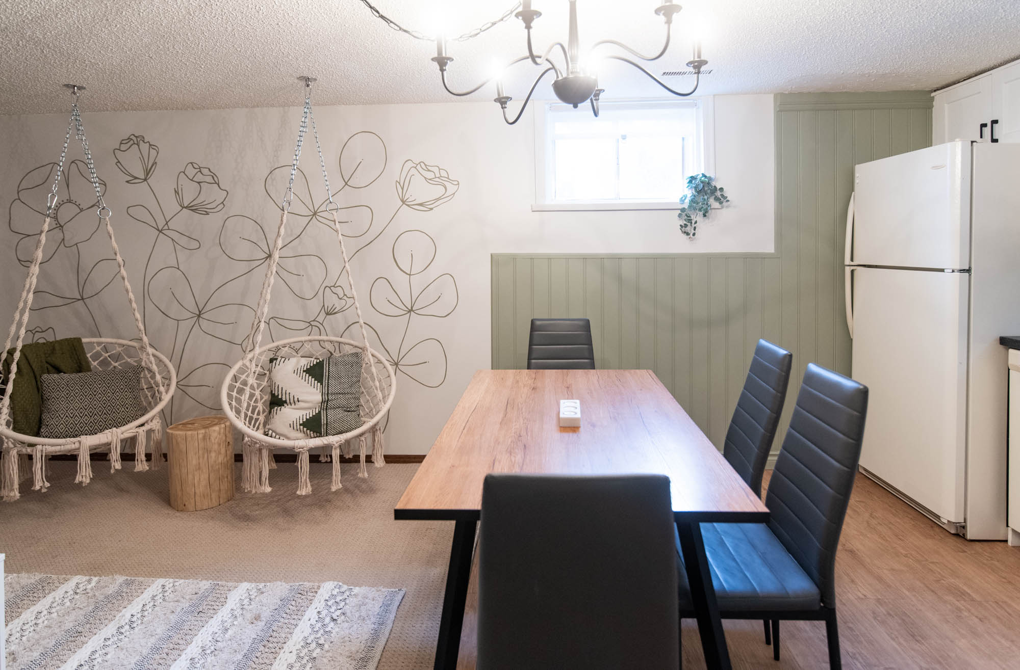Playful basement suite AirBnB with farmhouse kitchen and hanging macrame chairs in front of a line art floral mural