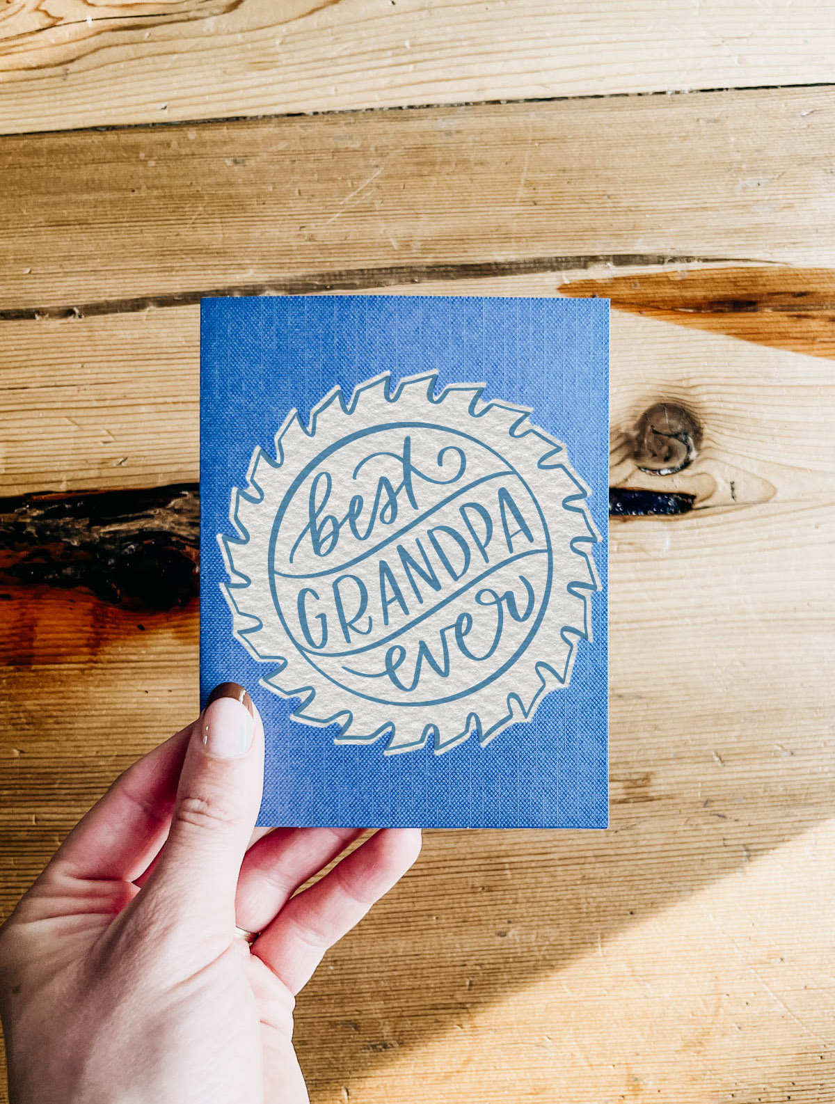 Best grandpa ever sawblade card made with free hand lettered SVG file held over wood table