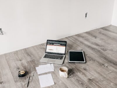 image of computer, measuring tape and papers spread out on floor of unfinished room.