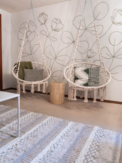 hanging chairs in front of a green floral line art mural