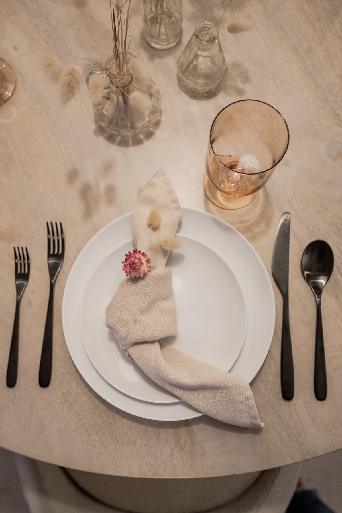 Simple fall table setting- tan napkin knotted on white plates with pink strawflower and bunny tail glasses