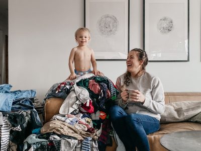 Sharing my laundry system- image of toddler on top of a pile of laundry while mom laughs