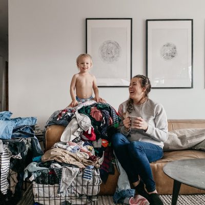 Sharing my laundry system- image of toddler on top of a pile of laundry while mom laughs