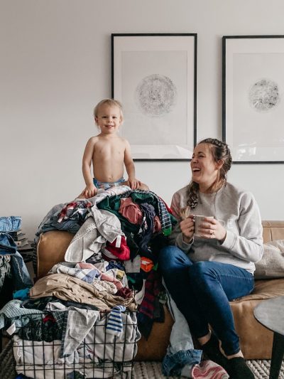 Sharing my laundry system- image of toddler on top of a pile of laundry while mom laughs