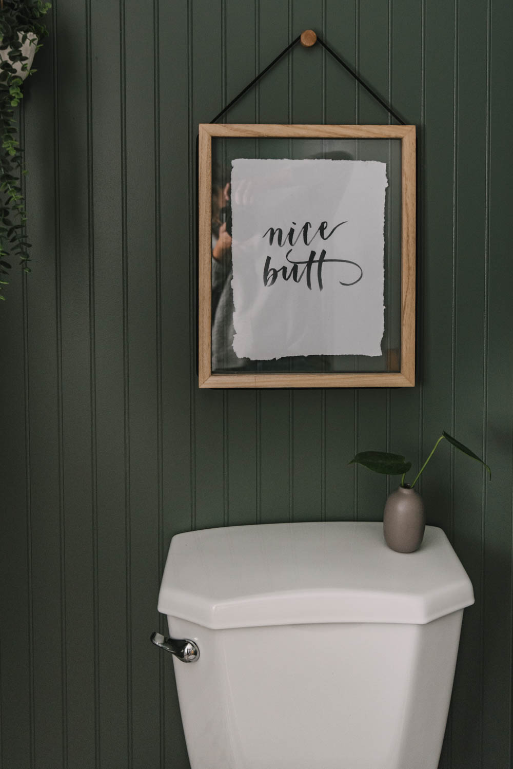 playful 'nice butt' wall art above a toilet in a dark green bathroom remodel