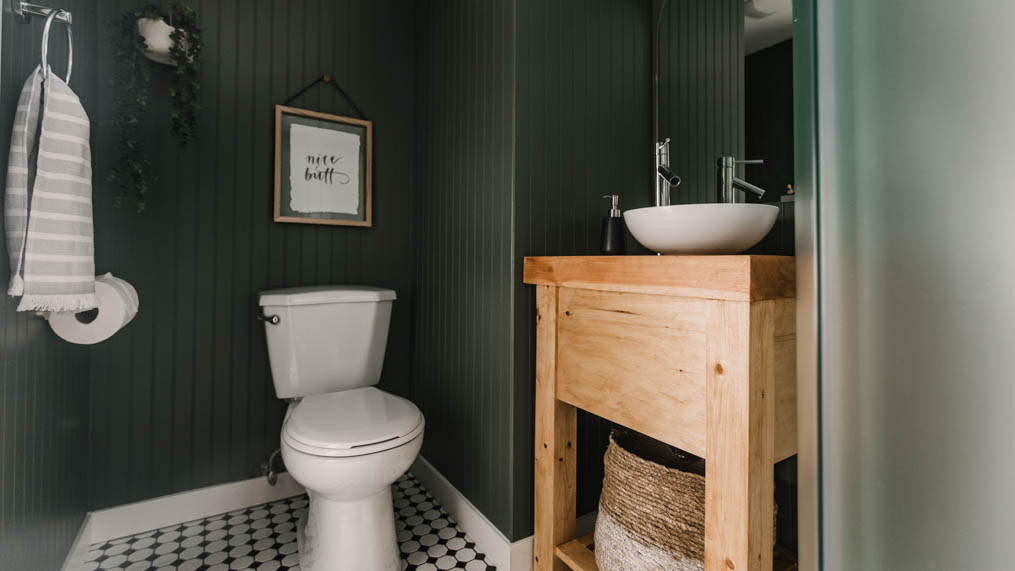 small bathroom makeover with green walls, black and white tile floor and wooden vanity