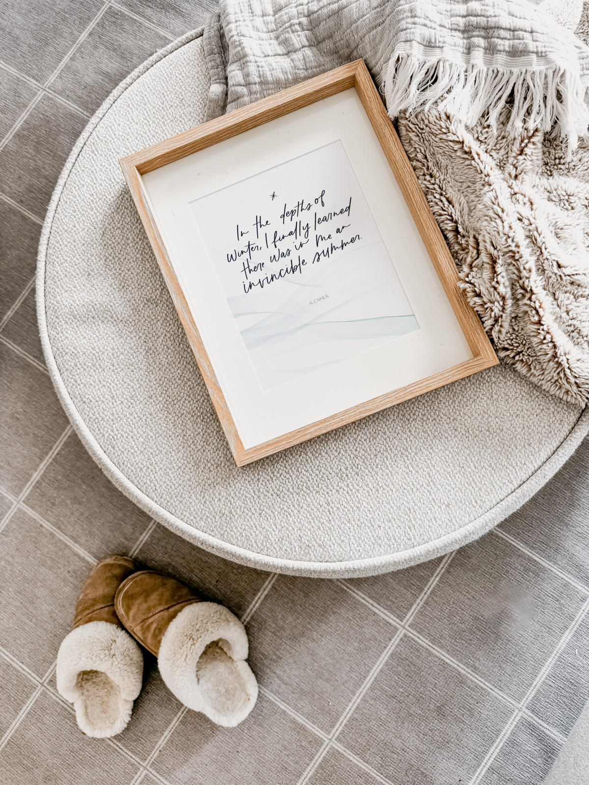 Free Printable Quote for Winter Decorating, shown framed on ottoman with blankets and slippers: in the depths of winter I finally learned there was in me an invincible summer