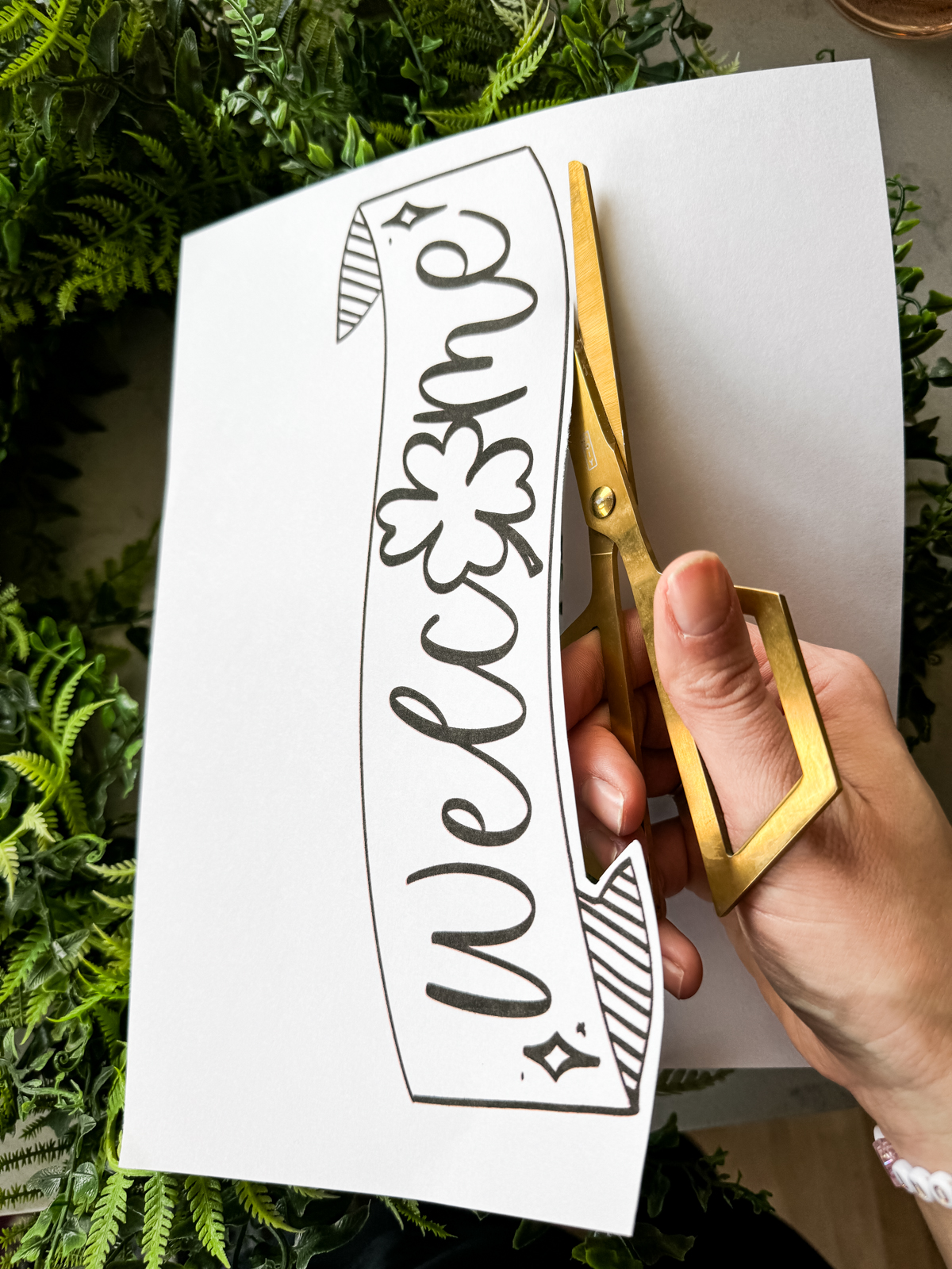 image of printed welcome banner (with O shamrock) being cut to size by gold scissors welcome banner is hand drawn with brush marker style and shamrock O