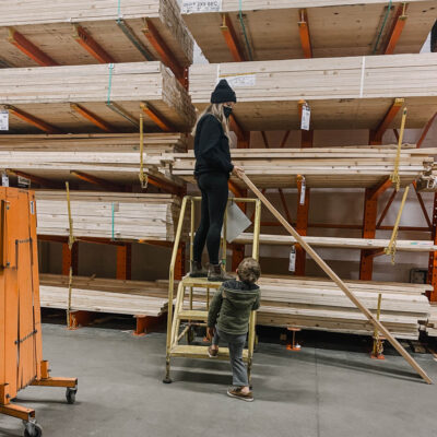 image of woman choosing wood in a hardware store lumber section by looking down the length of a board for warping image from blog post thats a introduction to the types of wood available for DIY projects