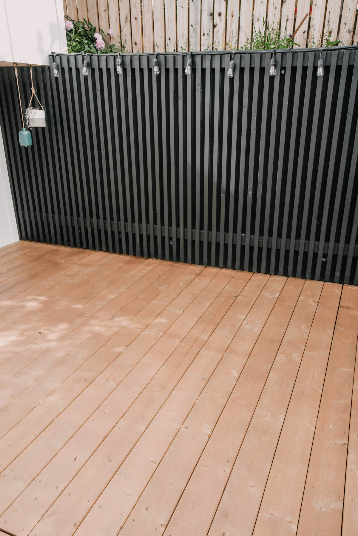 image shows outdoor space with three different wood finishes: Wooden deck is stained pressure treated wood, wood slat retaining wall cover is SPF and wooden fence is aged untreated cedar