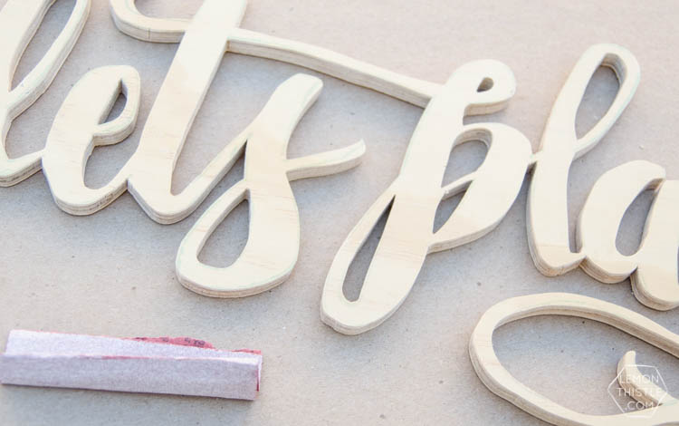 image of plywood cut into hand lettered shape with a scroll saw, being sanded